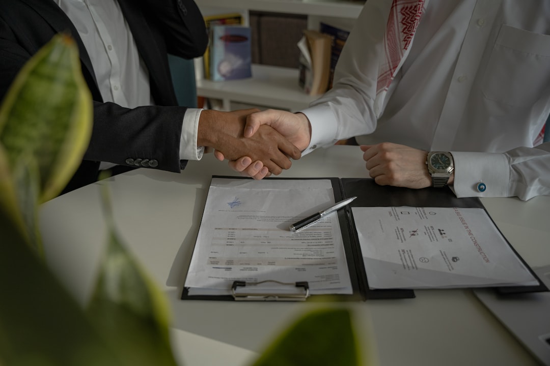 Two people shaking hands over a signed agreement on a desk