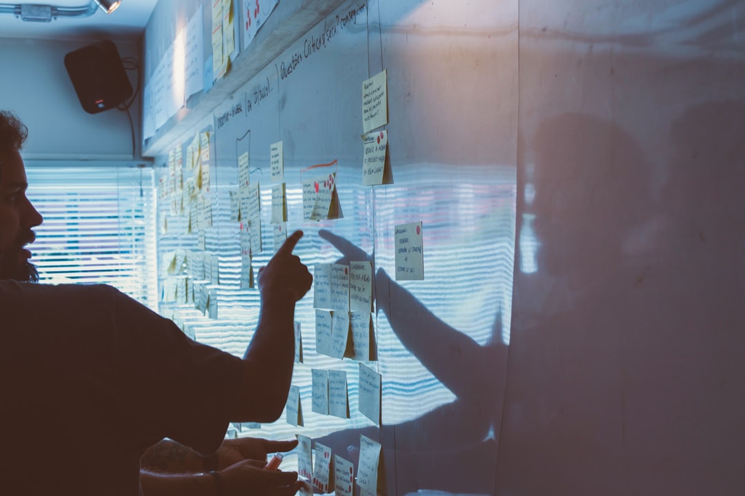 A strategist mapping a plan across sheets of paper on a wall while a colleague points to a step in the sequence